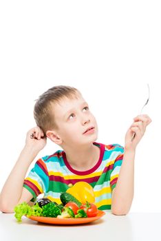 portrait of a boy at the table with a plate of vegetables for lunch, isolated on white background