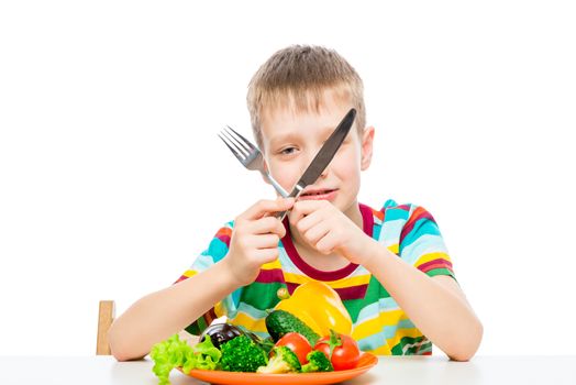 boy with a knife and fork eating fresh raw vegetables, portrait isolated