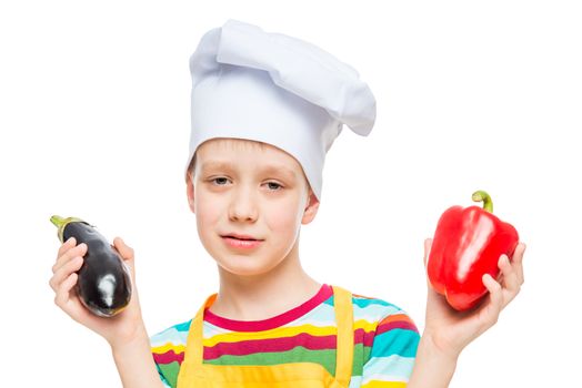 portrait of a child in a cook hat with pepper and eggplant on a white background