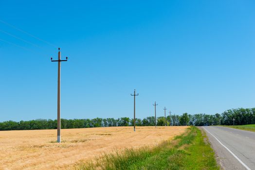 motor road and wheat field with electric pylons, rural landscape