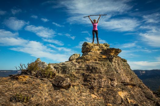 Woman after climbing a challenging mountain raises her arms in victory in Gardens of Stone National Park.