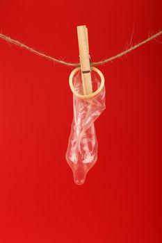 Close up one condom hanging on twine washing line with wooden clothespin over red background with copy space, low angle side view