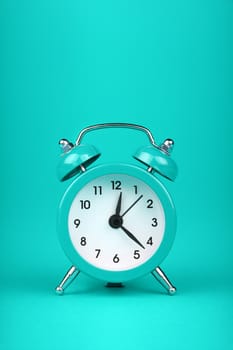 Close up one small teal blue metal twin bell retro alarm clock over aqua turquoise paper background with copy space, low angle front view
