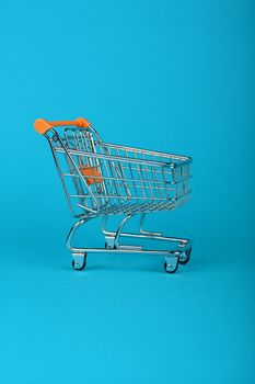 Close up empty toy metal supermarket shopping cart over pastel blue background with copy space, low angle side view