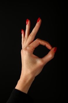 Woman hand with red nails showing okay, like or good gesture isolated on black background, side view