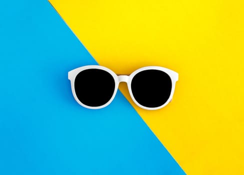 Sunny stylish white sunglasses on a bright blue-cyan and yellow-orange background, top view, isolated. Copy space. Flat lay.