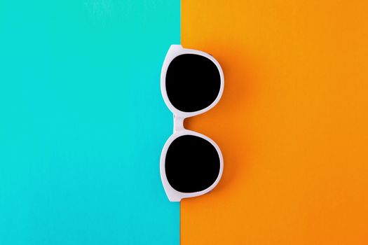 Sunny stylish white sunglasses on a bright blue-cyan and yellow-orange background, top view, isolated. Copy space. Flat lay.