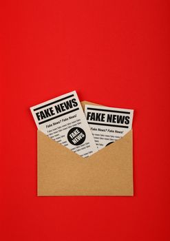 Close up brown paper mail envelope with FAKE NEWS newspapers over red background with copy space, elevated top view, directly above