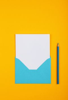 One open blank pastel blue envelope with white paper and wooden pencil over vivid yellow background, flat lay, directly above