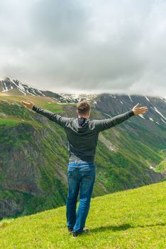A man who admires the beautiful mountain peaks, view from the back with arms outstretched