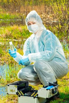 Ecologist woman in protective clothing with a flask for a water test on the lake