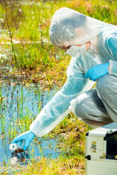 Ecologist woman in protective clothing takes samples of forest lake water