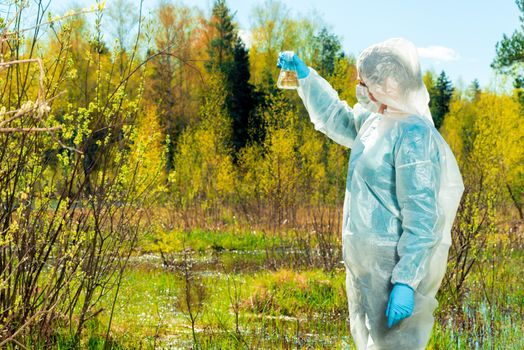 a researcher chemist-environmentalist conducts a visual inspection of water from a forest pond