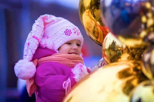 Portrait of the little girl who looks in reflection of a New Year's sphere on the street