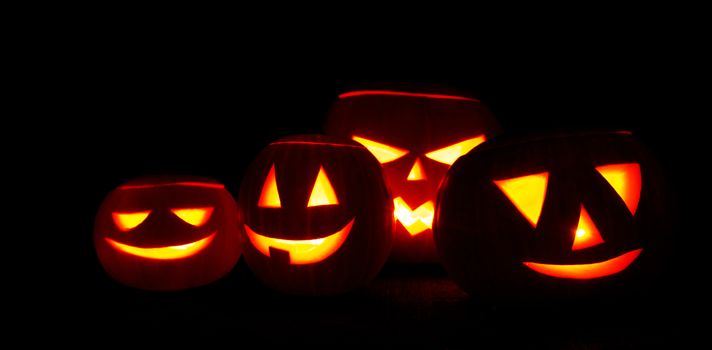Many Halloween Pumpkin glowing faces in a row on dark background