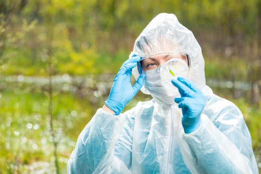 chemist researcher in protective clothing examines infected plants from a forest lake