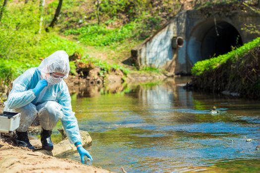 Scientist in protective suite taking water samples from the river
