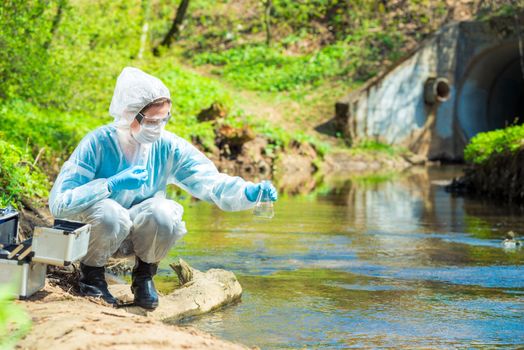 Environmental scientist with a flask takes a sample of water at the site of industrial discharge of water