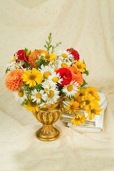 Vase with a bouquet of flowers and books on a fabric background