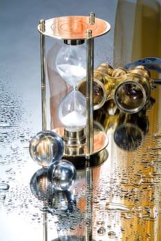 Hourglass and binocular on a glass background