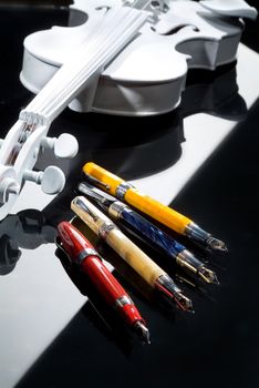 Four different pens and violin on a glass background