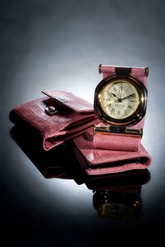 Travel clock and leather wallet on a glass studio background