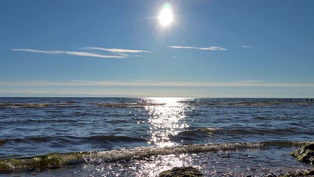 Sunny path reflection on the sea water, light surf on the beach.