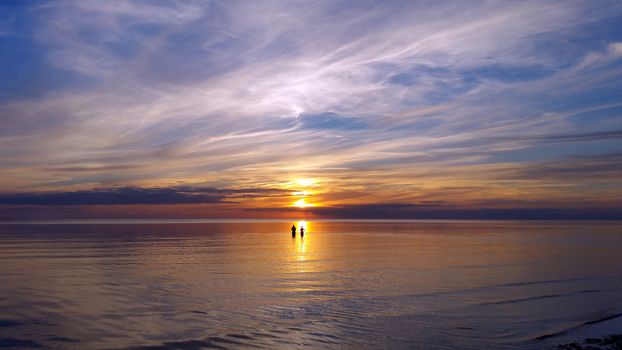 On the reflection of the sun in the sea, silhouettes of people are visible, during a magnificent color sunset reflecting in the water.