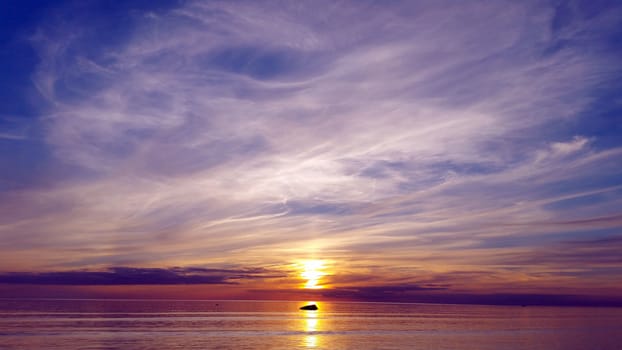 Beautiful multicolored sunset over sea. stone lies on a sunny path reflecting the sunset in the sea.