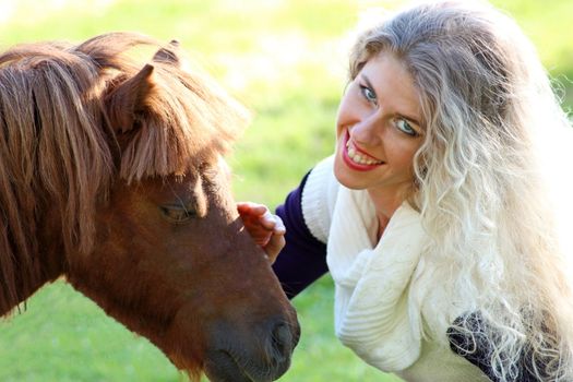 funny blonde girl strokes pony muzzle. Close-up