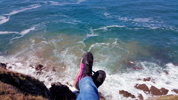 Sitting on the edge cliff. Top view from the cliff to the feet above the surf