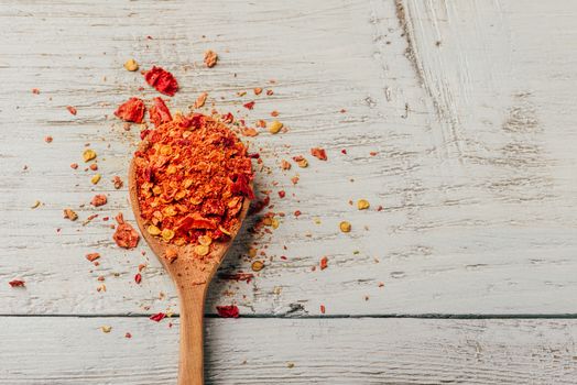 Spoonful of crushed red chili pepper over wooden background