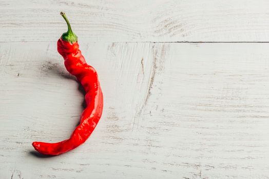 One red chili pepper over light wooden background.