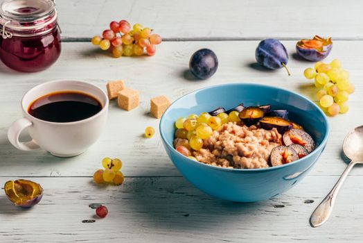 Healthy breakfast concept. Porridge with fresh plum, green grapes and cup of coffee. Ingredients over wooden background.