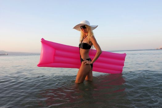 Blonde girl in white hat and sunglasses lie on the pink inflatable mattress on Red sea water