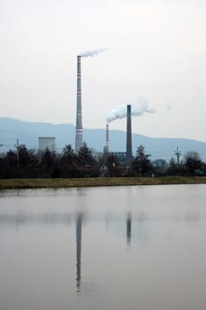 view of the chimneys with white smoke, reflected in the water against the backdrop of the mountain pass in the evening.