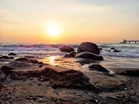 view of the sea with small waves and rocky shore, sunrise reflected in the water.