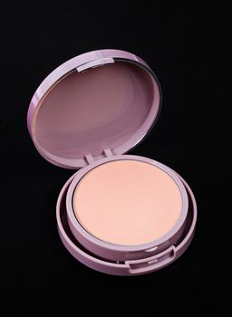 Face powder for makeup in pink container isolated on black background.