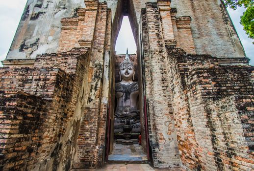 Sukhothai Historical Park, Thailand, traveller with ancient Buddha statue at Wat Si Chum temple.