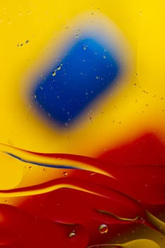 Abstract oil spots in motion on water on blurred yellow background. Red and blue spots on blurred background. Photo with small depth of field.