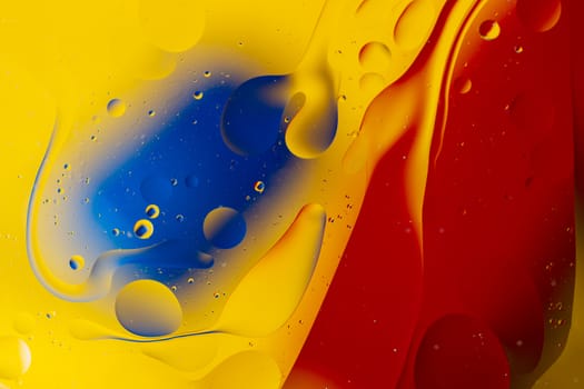 Abstract oil spots in motion on water on blurred yellow background. Red and blue spots on blurred background. Photo with small depth of field.