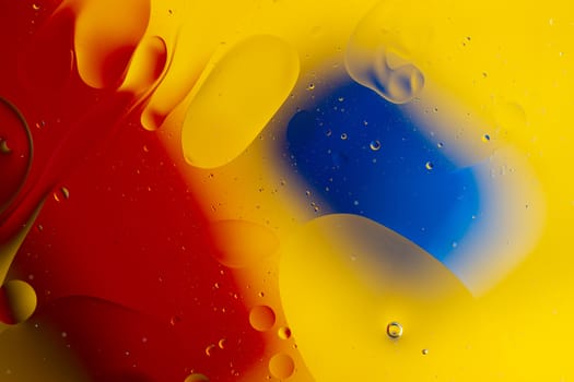 Abstract oil spots in motion on water on blurred yellow background. Red and blue spots on blurred background. Photo with small depth of field.