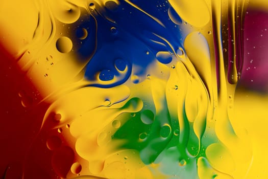 Abstract oil spots in motion on water on blurred yellow background. Red, green, purplee and blue spots on blurred background. Photo with small depth of field.