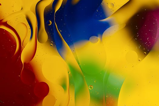 Abstract oil spots in motion on water on blurred yellow background. Red, green, purplee and blue spots on blurred background. Photo with small depth of field.