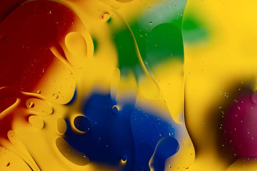 Abstract oil spots in motion on water on blurred yellow background. Red, green, purplee and blue spots on blurred background. Photo with small depth of field.