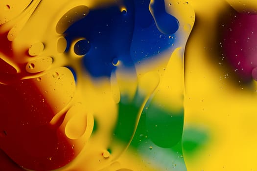 Abstract oil spots in motion on water on blurred yellow background. Red, green, purplee and blue spots on blurred background. Photo with small depth of field.