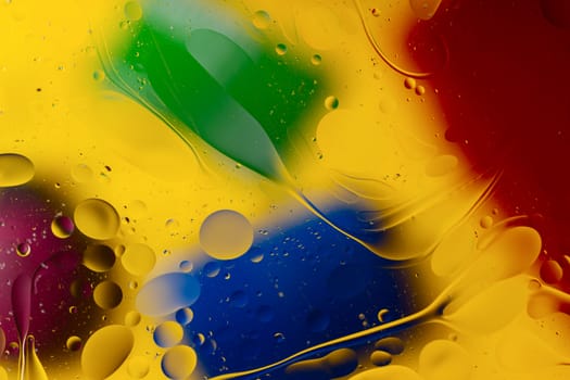 Abstract oil spots in motion on water on blurred yellow background. Red, green, purplee and blue spots on blurred background. Photo with small depth of field.