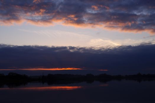 Red evening sunset above the lake or river. Purple and blue clouds and falling sun