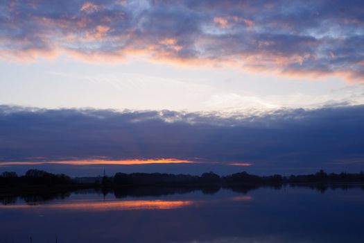 Red evening sunset above the lake or river. Purple and blue clouds and falling sun