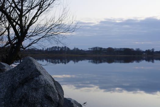 Gray evening sunset above the lake or river. Blue clouds on horizon